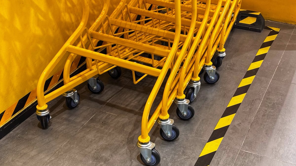 Stacked bright yellow shopping trolleys on a grey floor with black-and-yellow hazard warning stripes
